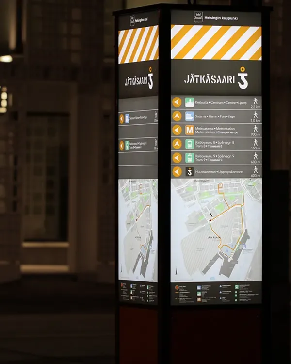 A Jätkäsaari wayfinding pylon with a service directory and maps in a city setting at night.